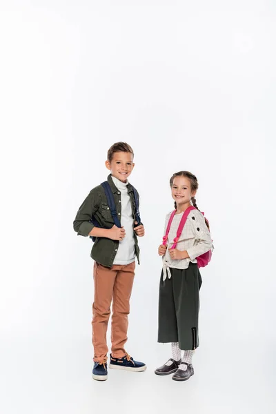 Cheerful schoolkids standing with backpacks isolated on white — Stock Photo