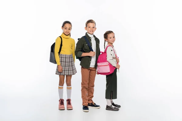 Cheerful schoolboy and schoolgirls standing with backpacks on white — Stock Photo