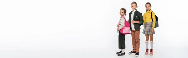 Fröhlicher Schuljunge und Schulmädchen stehen mit Rucksäcken auf weißem Transparent — Stockfoto