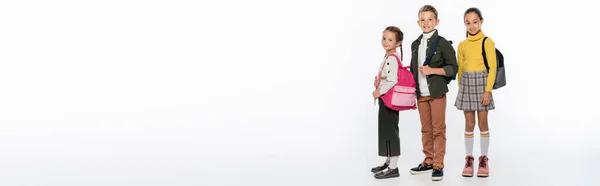 Alegre colegial y colegialas de pie con mochilas en blanco, pancarta - foto de stock