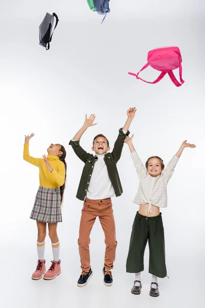 Fröhliche Schüler und Schulmädchen werfen Rucksäcke auf weiße — Stockfoto