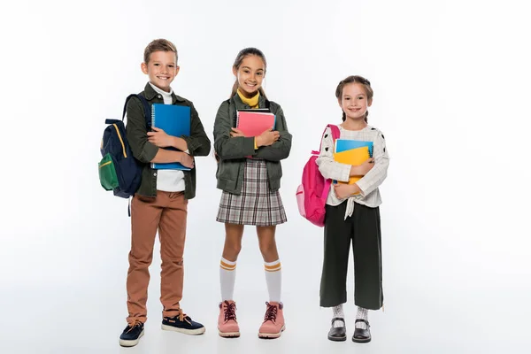 Cheerful schoolboy and schoolgirls standing with backpacks and notebooks on white — Stock Photo
