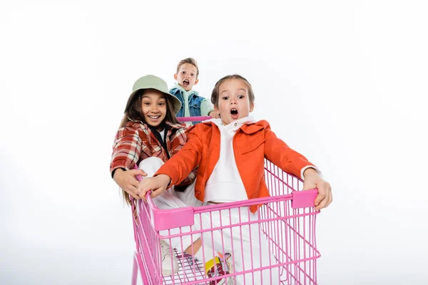 Crianças alegres montando no carrinho de compras rosa no branco — Fotografia de Stock