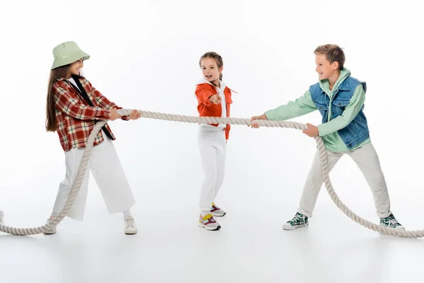 Preteen kid looking at friends pulling rope while playing tug of war game on white — Stock Photo