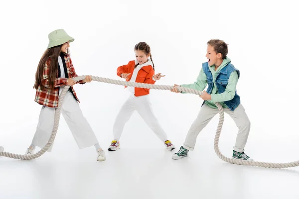 Preadolescente niño gesto cerca de amigos tirando de la cuerda mientras juega tirón de juego de guerra en blanco - foto de stock