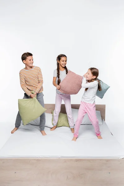 Cheerful kids having pillow fight while standing on white — Stock Photo