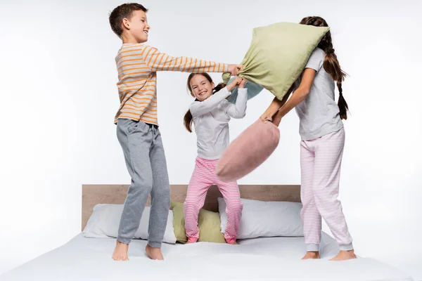 Joyeux enfants ayant bataille d'oreillers tout en se tenant isolé sur blanc — Photo de stock
