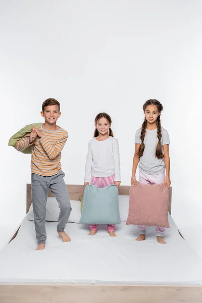 Joyful kids standing on bed with pillows isolated on white — Stock Photo