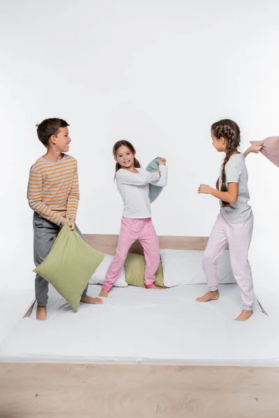 Crianças felizes tendo travesseiro luta enquanto de pé isolado no branco — Fotografia de Stock