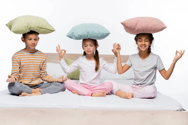 Crianças felizes com travesseiros na cabeça meditando isolado no branco — Fotografia de Stock