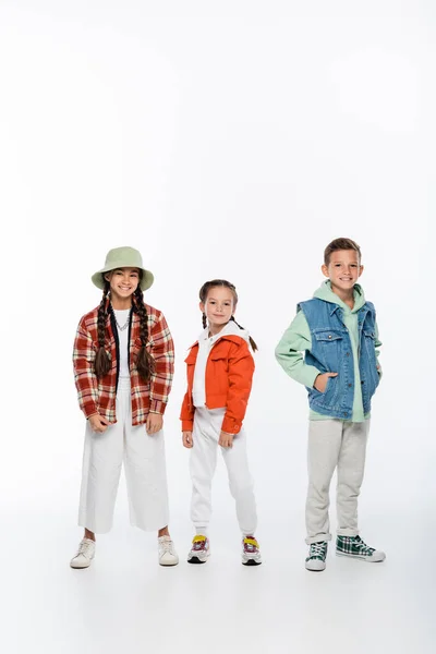 Full length of cheerful boy and stylish girls posing on white — Stock Photo