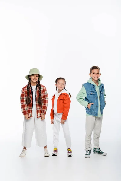 Comprimento total de menino alegre e meninas elegantes posando no branco — Fotografia de Stock