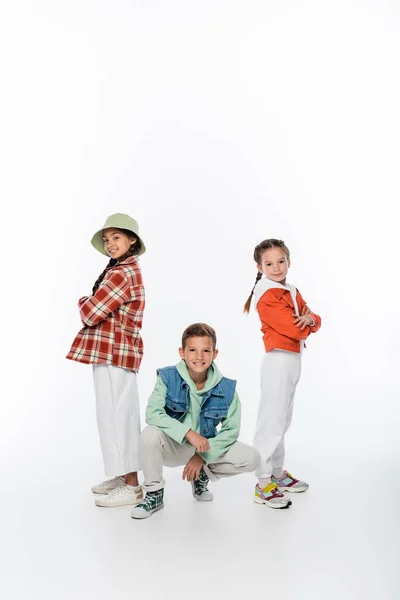 Longitud completa de los niños elegantes sonriendo mientras posan en blanco - foto de stock