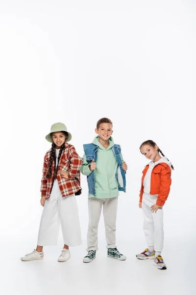 Longitud completa de los niños de moda sonriendo mientras posan en blanco - foto de stock