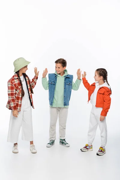 Full length of stylish kids smiling while giving high five on white — Stock Photo