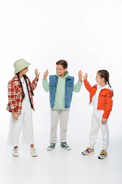 Longitud completa de los niños con estilo sonriendo mientras que da cinco alto en blanco - foto de stock