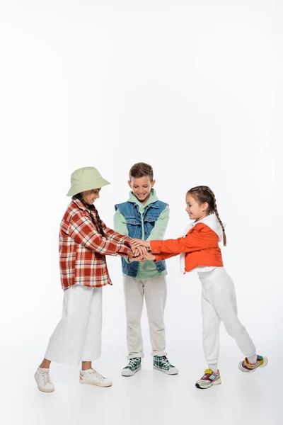 Comprimento total de crianças elegantes sorrindo enquanto segurando as mãos juntas no branco — Fotografia de Stock