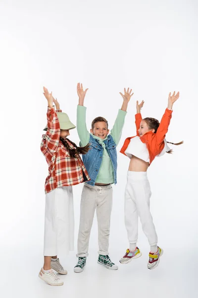 Full length of stylish kids smiling while posing with raised hands on white — Stock Photo
