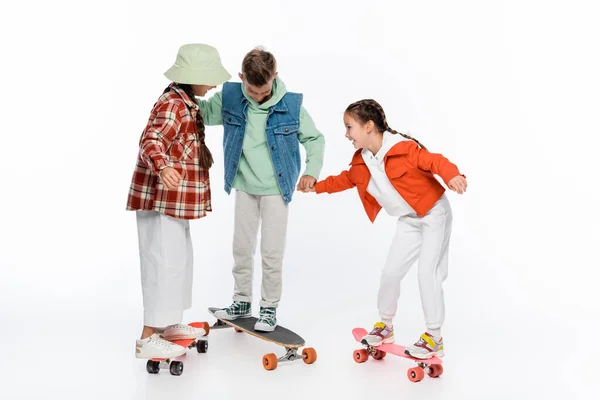Longitud completa de los niños de moda sonriendo mientras monta longboard y penny boards en blanco - foto de stock
