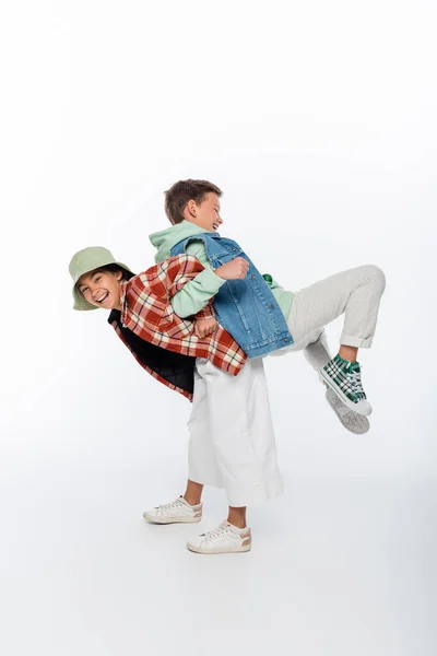 Comprimento total da menina feliz no chapéu panama piggybacking menino alegre no branco — Fotografia de Stock