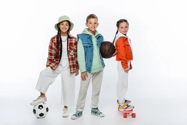 Feliz niños con bolas cerca amigo montar penny board en blanco - foto de stock