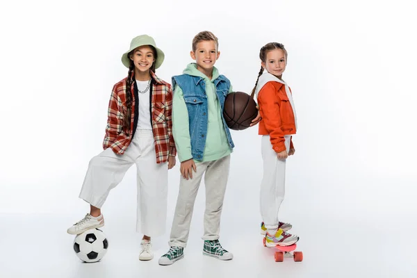 Happy kids with balls near friend riding penny board on white — Stock Photo
