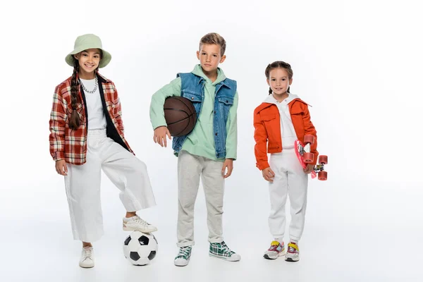 Happy kids holding balls near friend with penny board on white — Stock Photo