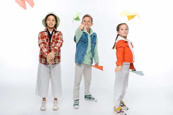Full length of joyful preteen kids throwing paper planes in air on white — Stock Photo