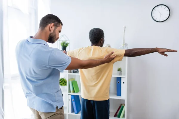 Rehabilitologist diagnosing mature african american man in clinic — Fotografia de Stock