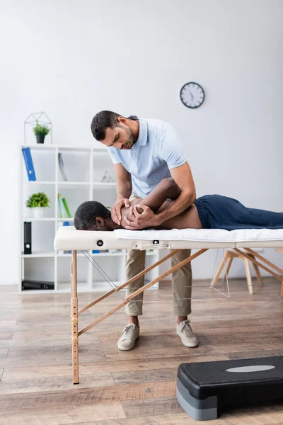 Fisioterapeuta estiramiento hombro de hombre afroamericano durante el procedimiento de rehabilitación - foto de stock