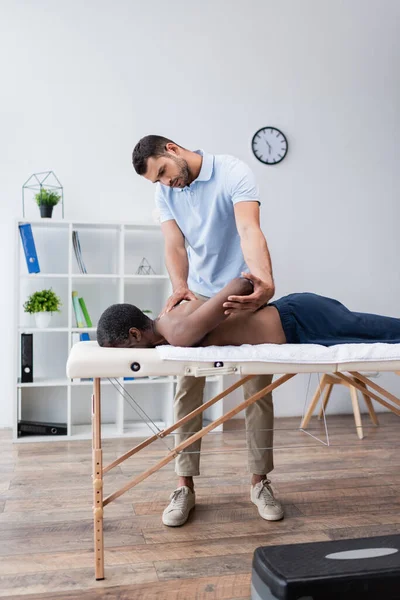 Young rehabilitation specialist stretching arm of african american man on massage table — Stock Photo