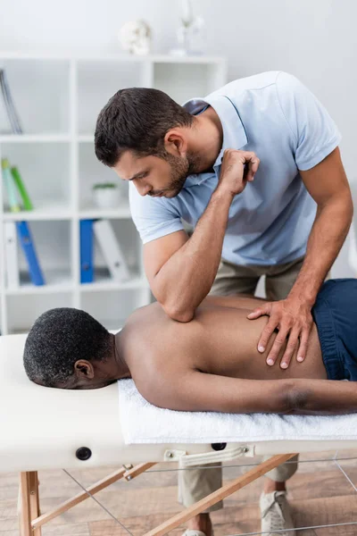 African american man lying on massage table during massotherapy in rehabilitation center — Fotografia de Stock