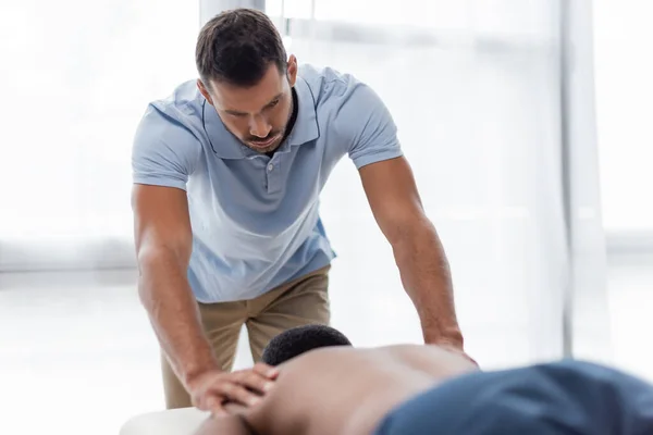 Masseur faire massage du dos à l'homme afro-américain flou dans le centre de réadaptation — Photo de stock