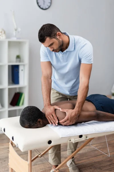 Physiotherapist massaging shoulder of middle aged african american man — Stock Photo