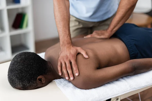 Africano americano hombre consiguiendo espalda y hombro masaje durante rehabilitación - foto de stock