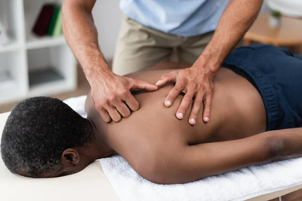 Rehabilitólogo tratamiento africano americano hombre mientras haciendo espalda masaje - foto de stock