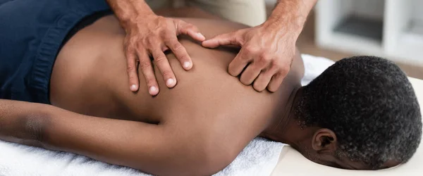 Хиропрактик, делающий массаж спины африканскому американскому пациенту в клинике, баннер — стоковое фото