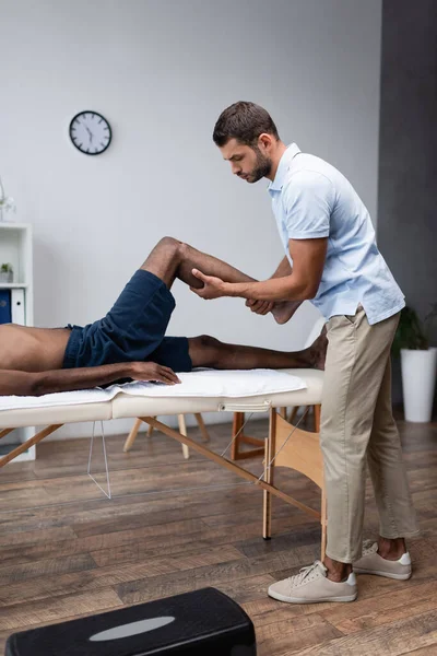 Physical therapist massaging leg of african american man in rehab clinic — Stock Photo