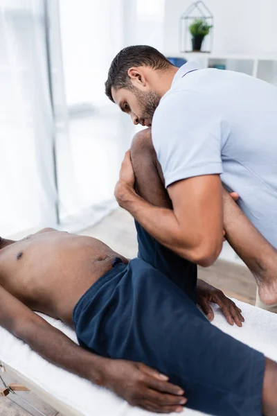 Réhabilitologue travaillant avec la jambe de l'homme afro-américain pendant le traitement de réadaptation — Photo de stock