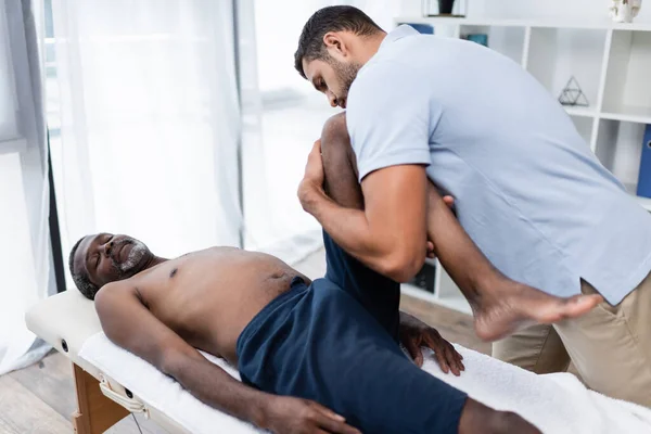 Хіропрактика розтягування ноги афроамериканського пацієнта під час фізіотерапії — стокове фото