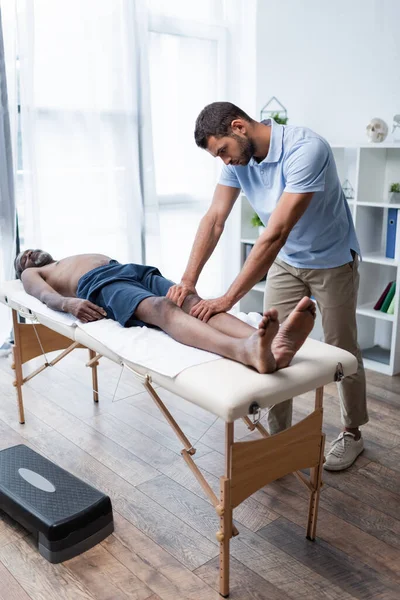 Full length view of mature african american man lying on massage table during massotherapy — Stock Photo