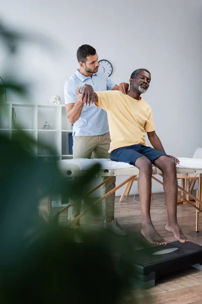 Young physiotherapist examining middle aged african american man on blurred foreground — Fotografia de Stock