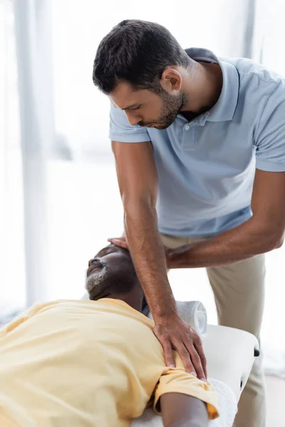 Fisioterapeuta tratando homem americano africano maduro no centro de reabilitação — Fotografia de Stock