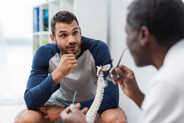 Молодий чоловік розмовляє з розмитим афроамериканським лікарем у реабілітаційному центрі — стокове фото