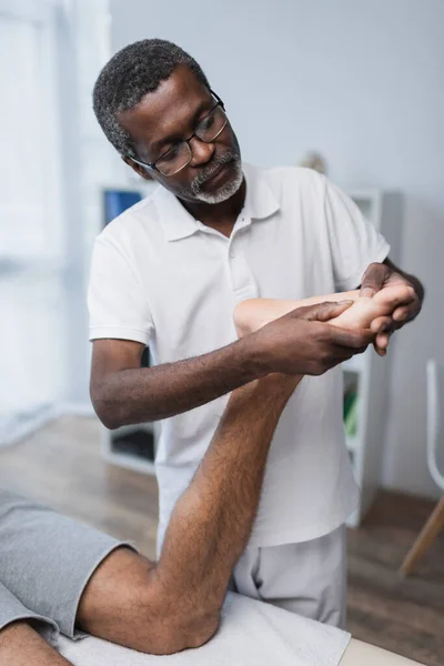 Moyen afro-américain kinésithérapeute massage pied de l'homme en centre de réadaptation — Photo de stock