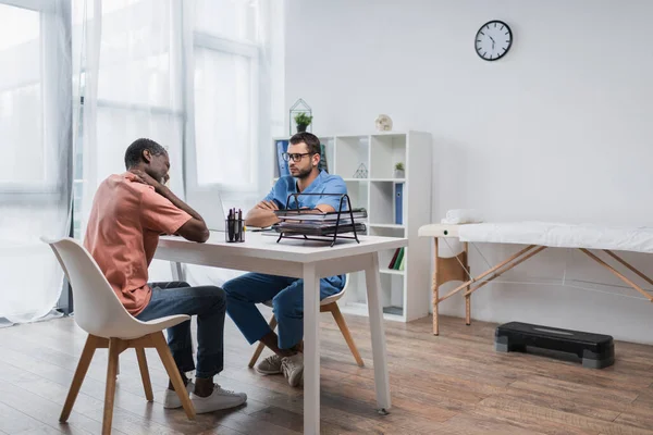 African american man suffering from neck pain on consultation with rehabilitologist — Stock Photo