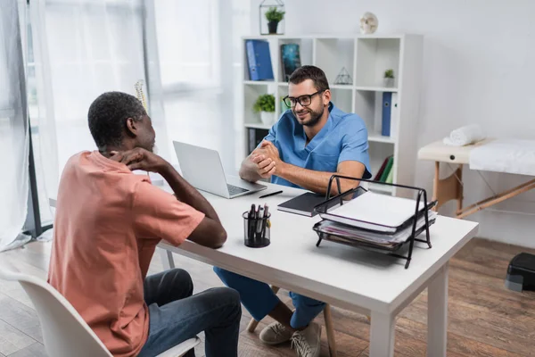 Homme afro-américain d'âge moyen touchant le cou lors d'une consultation avec un physiothérapeute positif — Photo de stock