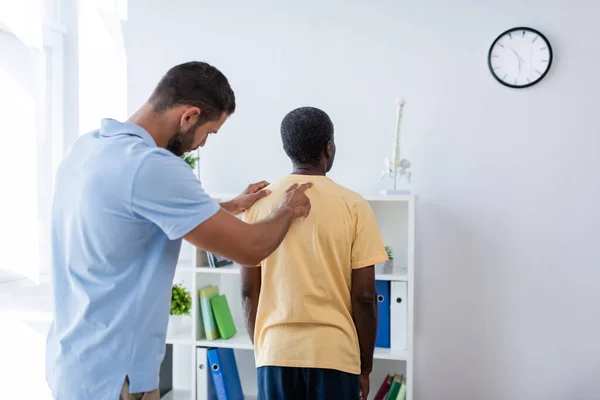 Médico examinando de volta do homem americano africano maduro no centro de reabilitação — Fotografia de Stock