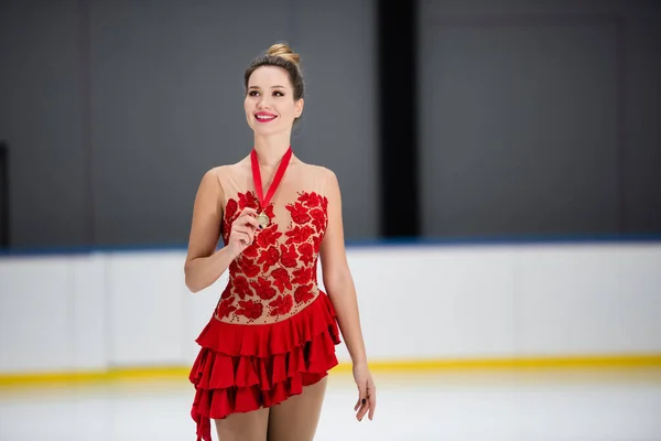 Smiling figure skater in red dress holding golden medal on ice arena — Stock Photo