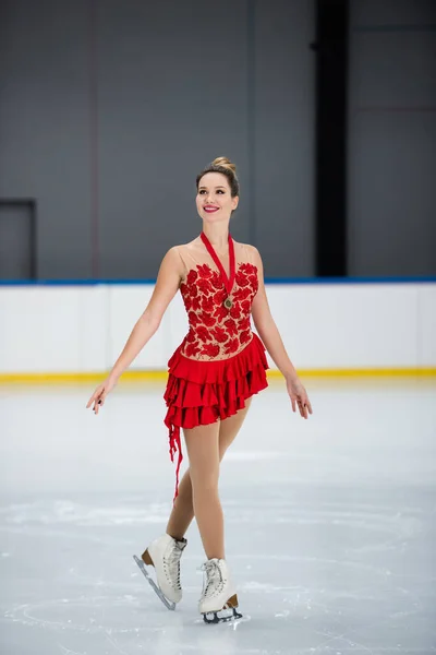 Comprimento total de patinador figura feliz em vestido vermelho com medalha de ouro patinação na arena de gelo — Fotografia de Stock